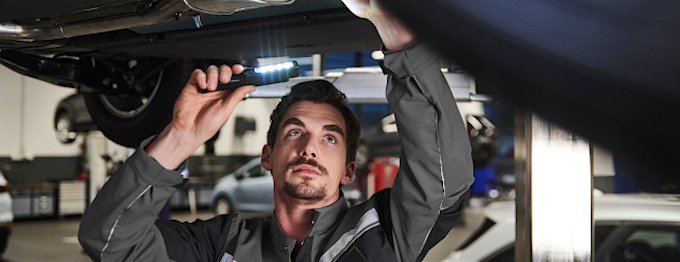 Mechaniker überprüft unter ein Auto mit einer Taschenlampe in einer Werkstatt.