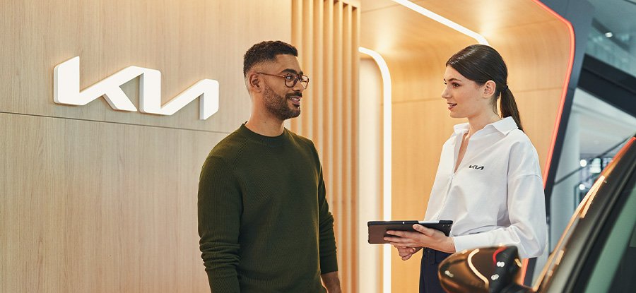 Mann und Frau im Kia-Autohaus, konsultieren ein digitales Gerät vor dem Kia-Logo.