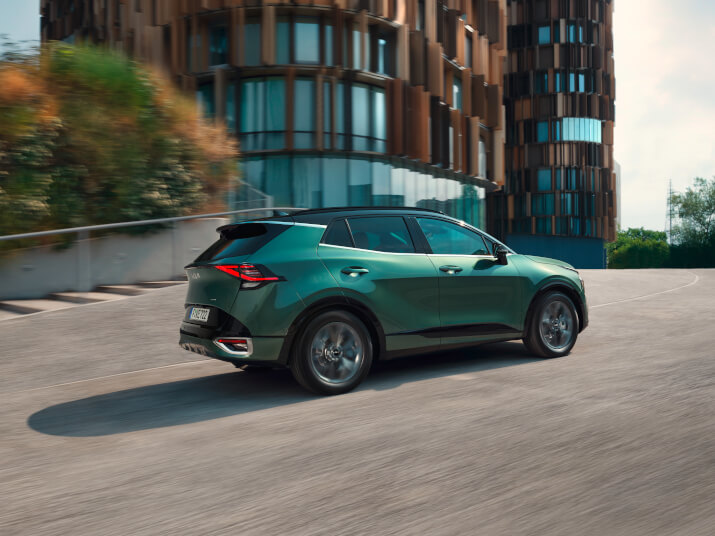 Ein grüner SUV fährt auf einem modernen Parkplatz mit einzigartiger Architektur im Hintergrund.