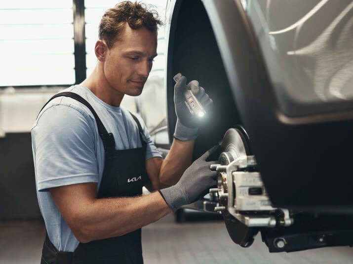 Mechaniker überprüft Bremssystem eines Autos mit Werkzeug und Taschenlampe in einer Werkstatt.