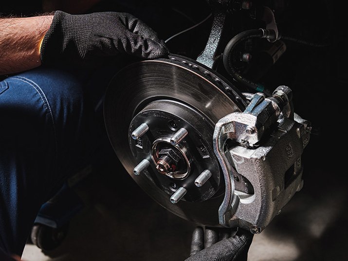 Ein Mechaniker arbeitet an einer Bremsanlage, greift die Bremsscheibe mit Handschuhen.