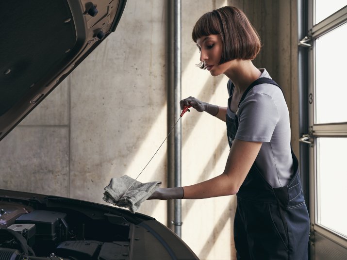 Eine Frau mit kurzer Frisur überprüft den Ölstand im Motor eines Autos in einer modernen Werkstatt.