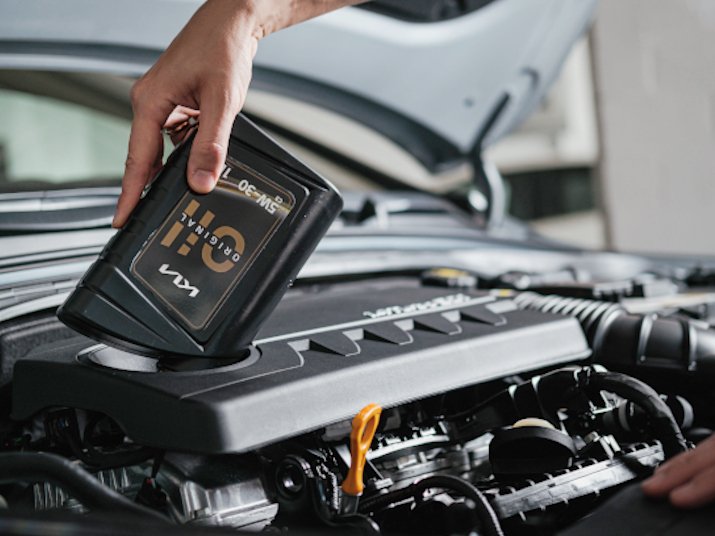 Eine Hand hält eine Ölflasche über einem Auto-Motor, um Öl nachzufüllen.