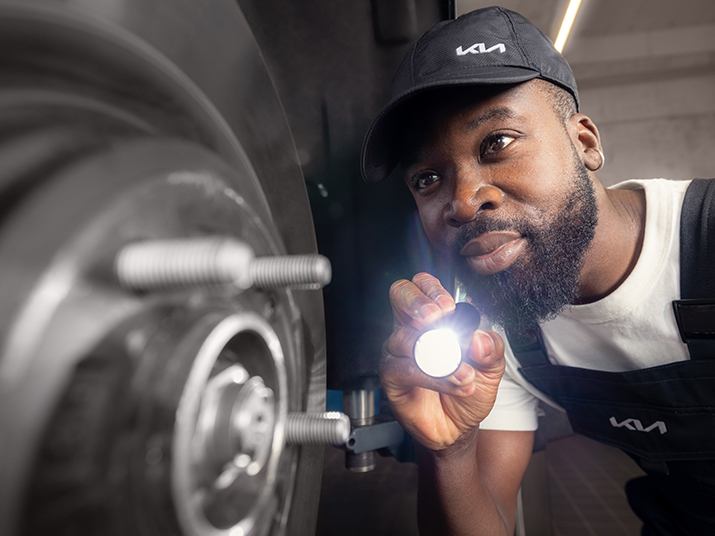 Mechaniker untersucht das Auto von unten mit Taschenlampe, während er auf die Reifen schaut.