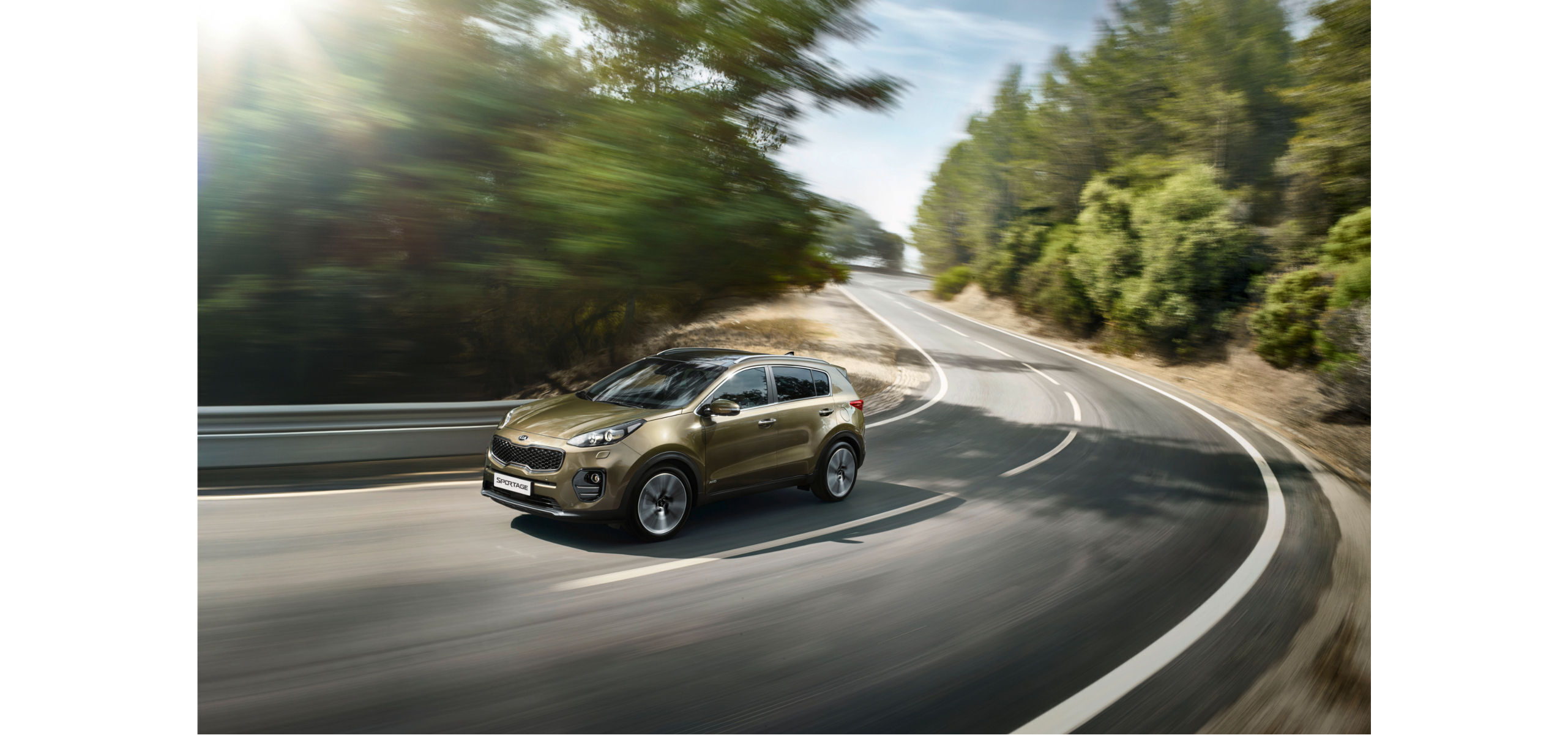 Ein goldfarbener SUV fährt dynamisch eine kurvenreiche Straße entlang, umgeben von Bäumen.